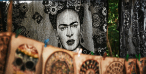 A black and white tapestry featuring a detailed portrait surrounded by floral and butterfly motifs, with colorful skull and circular artworks hanging on a line in the foreground.